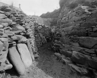Passage between broch wall (right) and larger circular dwelling (left)