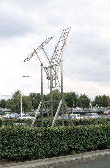 View of sculpture 'Strange Attractor 3', in triangular area enclosed by hedge in Gyle Shopping Centre carpark.