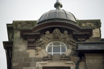 View of top of NE corner of building, showing cherubs supporting a bearded head.