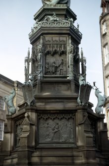 View of SE side of pedestal of Monument to the Duke of Buccleuch, showing bronze panels. The upper panel shows the anniversary dinner given by the tenantry of the Duke in Edinburgh in 1878; the lower panel shows the burning of Branxholm by the English in 1532.