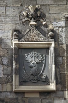 View of carved frame containing shield, with inscription panel and thistles above, between first floor windows of 165 Canongate.