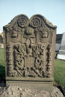 General view of gravestone of Margaret Hill, 1754. Rosettes, crown over crossed palm fronds and vine, double winged souls and pair of double torches. Foliate crest Insc: 'R.H K.M'. Emblems of mortality linked by ribband. (skulls, arrows of Death, hourglass and crossed bones). 
