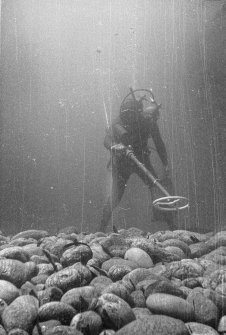 A diving archaeologist conducting a metal-detector survey in Gulley B. The rounded boulders in the foreground are typical of the fill of gulleys on the Adelaar wreck-site, indicative of the dynamic environment which moves them around.