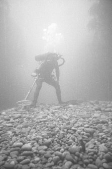 A diving archaeologist conducting a metal-detector survey in Gulley B. The rounded boulders in the foreground are typical of the fill of gulleys on the 				Adelaar wreck-site, indicative of the dynamic environment which moves them around. Weed growing on the vertical sides of the gulley is visible to left and right.