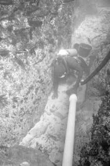Excavating a narrow gulley using a suction dredge. Note the bucket behind the archaeologist, used to carry away larger stones.