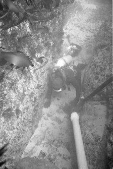 Excavating a narrow gulley using a suction dredge. Note the bucket behind the archaeologist, used to carry away larger stones.