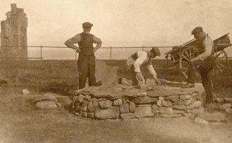 Scanned copy of photograph of John Nicolson and other men building a stone circle at New Keiss Castle gardens, with old Keiss Castle in the background