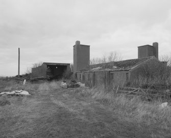 View N showing a small brick and concrete hut with motor transport shed to the rear.  Two water tank towers are visible in the background.
