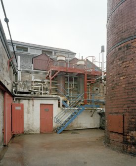 View from SW of two still condensers on the SW side of the still house, with the base of the boilerhouse chimney (right)