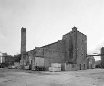 View from NW of W end of boiler-house range, with former still house in foreground, and chimney (left)