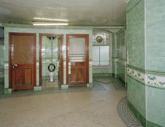 Interior. View one of two blocks of three cubicles.  All the original water closets and cisterns appear to have been removed, but most cubicles retain the green tilework.  Also visible (right) is a surviving stained-glass window.