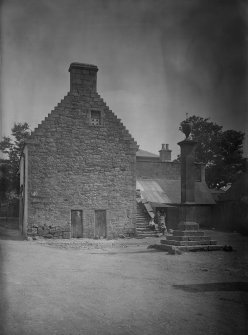 View of gable end of crowstepped building and mercat cross, Carnwath.
