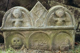 View of part buried headstone dated 1724, with angels and coulter,Clackmannan churchyard.
