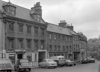 View of south elevations of 10 -16 Canongate, Jedburgh from west, showing the premises of John Luhn & Son, Matthew C Noble and J C Clark & Co