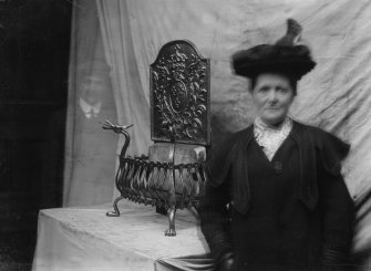 Photograph of a woman beside a wrought iron fender with man in background