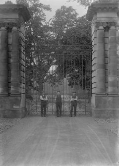 View of three men in front of Hopetoun House entrance gates with heraldic design and the date 1893