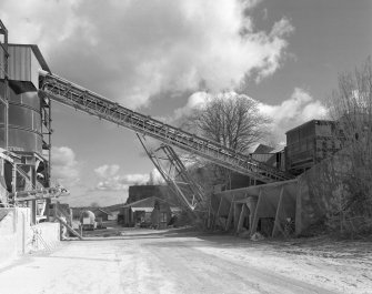View from W showing overhead conveyor from primary crusher (base visible to right) to former shaft kilns (now storage hoppers to left).  The supporting strut for the conveyor is a surviving portion of one of the original conveyors supplying the shaft kilns