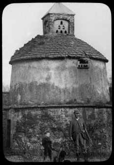 View of the Congalton dovecot showing the glover and flight holes, and with a young boy and a man with a gun in the foreground.
