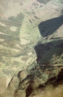 Oblique aerial view of the valley of the Eweslees burn with Ewes Doors in the foreground (c400m OD) and Eweslees farmstead in the distance (c200m OD) to the SE. The Roman watch tower is visible as a circular earthwork at the bottom of the image, and fragments of old trackways can be seen crossing the pass and heading into the valley below, while a series of linear earthworks run across the pass. 

