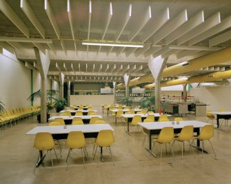 Interior view within works canteen, showing yellow plastic seats (chosen to match overhead ducts), and reinforced concrete beams and columns.

