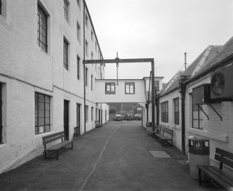 View from W along passage between offices and single storeyed sheds, right, and high mill, left.