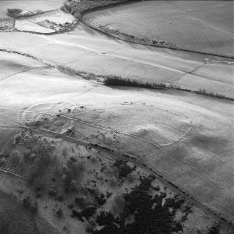 Oblique aerial view centred on the remains of the fort, settlement and cairn, taken from the NE.