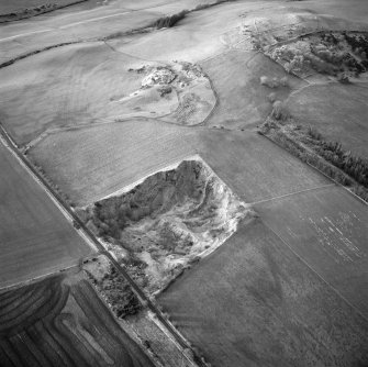 Oblique aerial view centred on the remains of the quarry with fort, settlement and cairn adjacent, taken from the ESE.