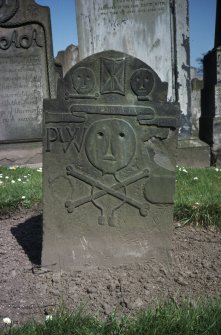 View of headstone 1711 to Patrick Wear, weaver, with primitive head and cross bones, and initials P W, Arbroath Abbey Churchyard.