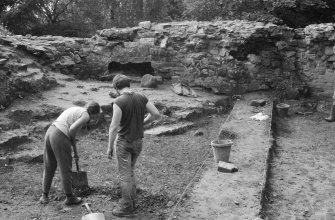 Excavation photograph : general view of ruins, rock face, and people working, looking west.