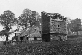 View of dovecot and cottages at St Clement's Wells, from W, with a woman standing by a fence.
