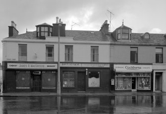 View of 41-47 Princes Street, Ardrossan, from SW, showing the premises of James R MacGregor chemist and druggist, an optician, a hairdresser and Cockburns dispensing chemist.