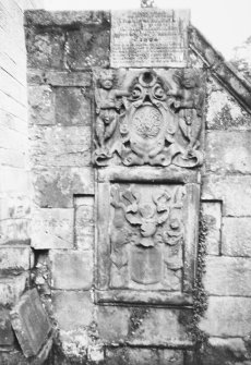 Edinburgh, Dell Road, Colinton Parish Church, Churchyard.
General view of a wall mounted grave stone in three sections. The top section bearing an inscription, the second carved with two putti holding an armorial crest and the third section showing another coat of arms.