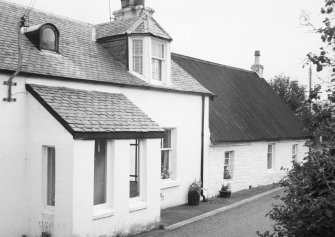 View of white-washed cottage and adjacent house.