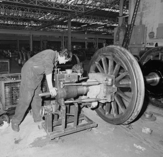 Glasgow, Springburn, St Rollox Locomotive Works, interior.
View of man removing a crane from a steam engine wheel.