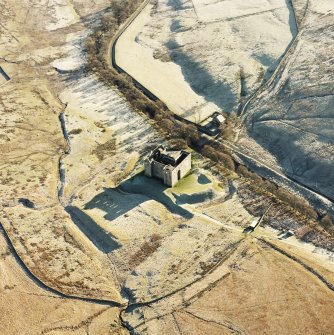 Oblique aerial view of Hermitage Castle centred on the remains of a castle and earthwork castle, taken from the NW.