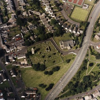 Oblique aerial view centred on the burial ground, belfry and clock tower with church and manse adjacent, taken from the S.