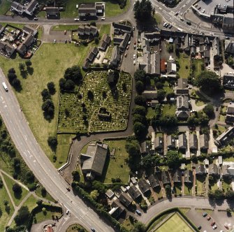 Oblique aerial view centred on the burial ground, belfry and clock tower with church and manse adjacent, taken from the ENE.