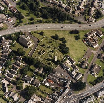 Oblique aerial view centred on the burial ground, belfry and clock tower with church and manse adjacent, taken from the NW.