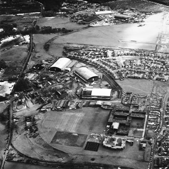 Oblique aerial view from NW, centred on three hangars and various other buildings.