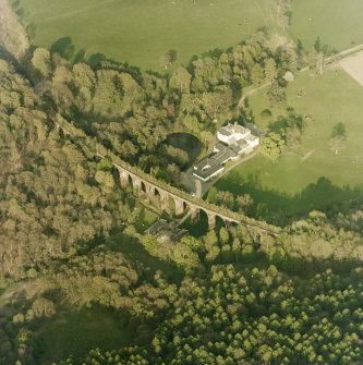 Oblique aerial view centred on the country house, railway viaduct and stables, taken from the W.