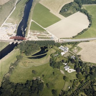 Oblique aerial view centred on the country house and garden with the lodge, railway viaduct and construction works adjacent, taken from the WSW.