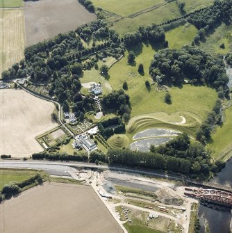 Oblique aerial view centred on the country house and garden with the lodge, railway viaduct and construction works adjacent, taken from the NE.