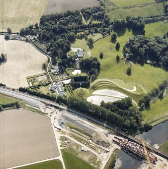 Oblique aerial view centred on the country house and garden with the lodge, railway viaduct and construction works adjacent, taken from the NE.