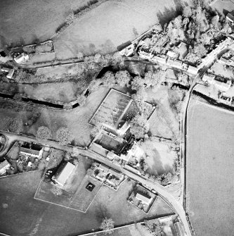 Oblique aerial view of Kirkgunzeon centred on the church, churchyard, manse and road bridge, taken from the SW.