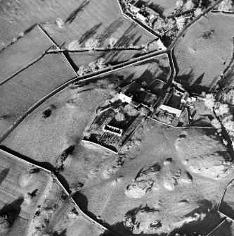 Oblique aerial view centred on the church, burial ground, manse and farmstead with smithy adjacent, taken from the SSE.