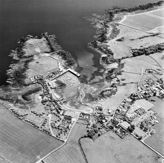 Oblique aerial view, taken from the N, centred on the village and harbour, and showing Isle Head fort and the remains of St. Ninian's Chapel in the top left-hand corner of the photograph.