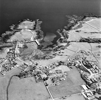 Oblique aerial view, taken from the N, centred on the village and harbour, and showing Isle Head fort and the remains of St. Ninian's Chapel in the top left-hand corner of the photograph.