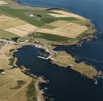 General oblique aerial view centred on the village, harbour, and the remains of the chapel and promontory fort, taken from the SSW.