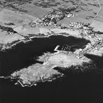 General oblique aerial view centred on the village, harbour, and the remains of the chapel and promontory fort, taken from the E.