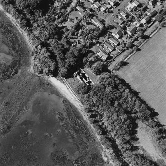 Oblique aerial view centred on the church and burial ground with pier adjacent, taken from the ESE.
